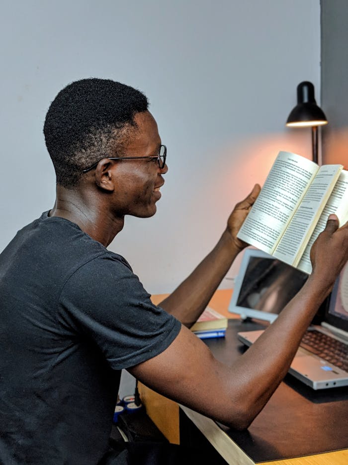 Home African man engaged in reading at a study desk, illuminated by a lamp.